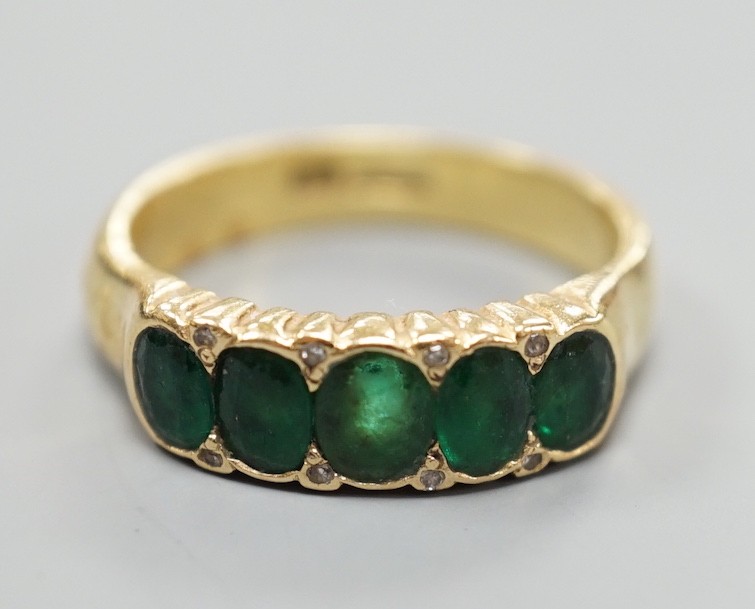 A modern 18ct gold and graduated five stone emerald set half hoop ring, with diamond chip spacers, size Q/R, gross weight 7.5 grams.